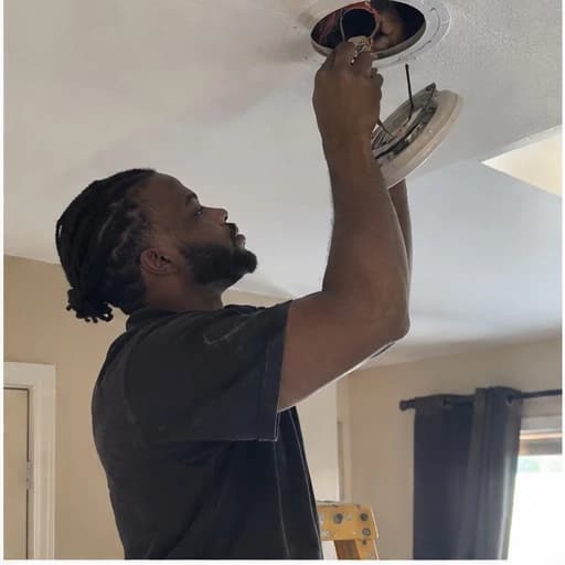 Electrician working on a ceiling fixture with its housing lowered for access.