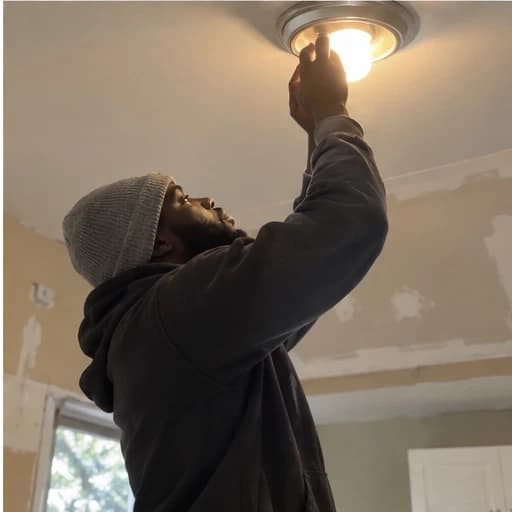 Electrician reaching up to a ceiling light fixture in a room under renovation.
